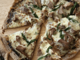 Smoked Duck with Hoisin Sauce Pizza on a wooden cutting board, with two fingers holding one slice